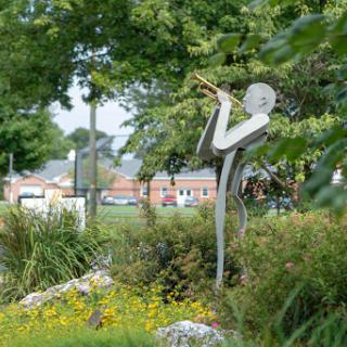 A striking sculpture of a musician playing the trumpet, surrounded by lush greenery in a park.