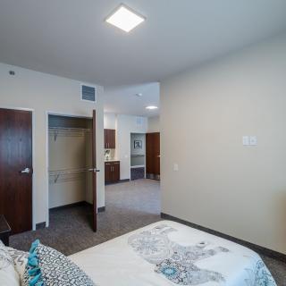 A modern bedroom with an open closet and view into the kitchen area.