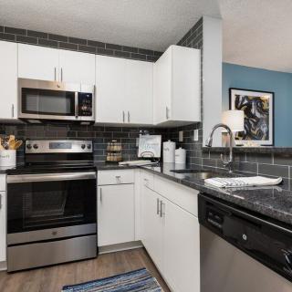 A modern kitchen with stainless steel appliances, white cabinets, and black countertops.