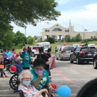 A joyful community parade celebrating seniors, with participants in wheelchairs enjoying colorful balloons.