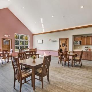 A spacious dining area with wooden tables and chairs, featuring a high ceiling and large windows.