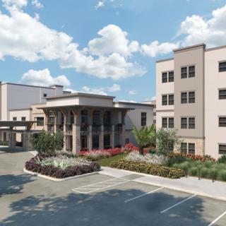 A modern building with a landscaped entrance and an adjacent parking area under a partly cloudy sky.