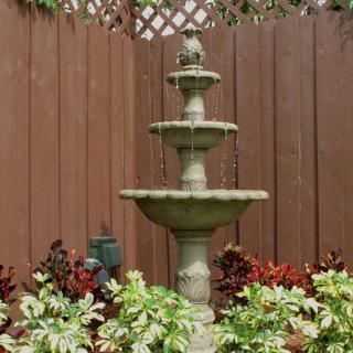 A tiered fountain surrounded by lush plants in a garden setting.