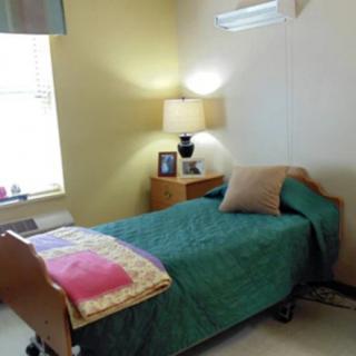 A cozy bedroom with a single bed, complete with a colorful quilt and pillows, illuminated by a bedside lamp.