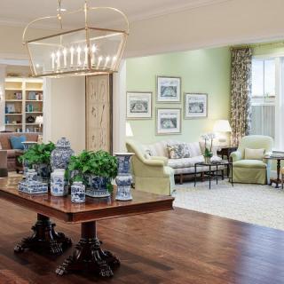 A beautifully designed living room featuring elegant furniture, a grand chandelier, and tasteful decor with potted plants on a hardwood floor.