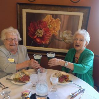 Two elderly women enjoying a meal and raising their glasses in a toast.