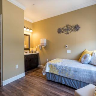 A cozy bedroom featuring a single bed, decorative wall art, and a vanity area with a mirror and lamp.