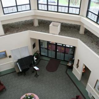 An aerial view of a spacious lobby featuring large windows, a piano, and comfortable seating arrangements.