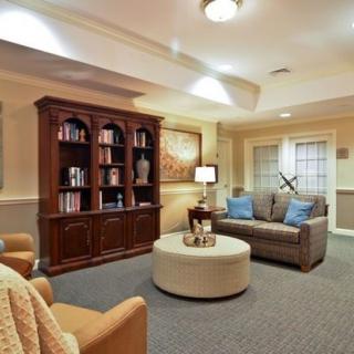 A cozy living room with a bookshelf, sofa, armchair, and warm lighting.