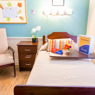 A well-organized nursing home room with a single bed, bedside table, and comfortable chair.