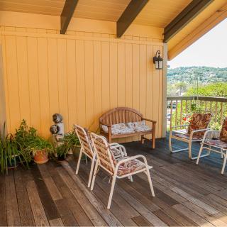 A cozy outdoor patio with wooden flooring, featuring several chairs and a bench surrounded by potted plants.