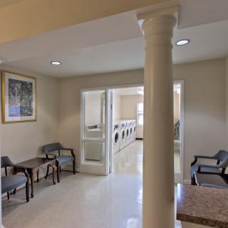 A well-lit laundry room with a waiting area, featuring chairs, tables, and a visible column.