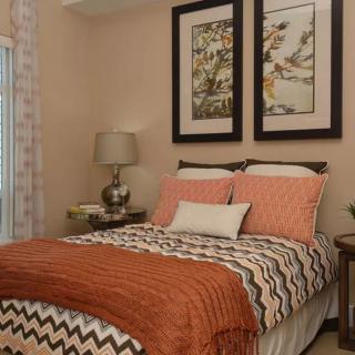 A cozy bedroom with patterned bedding, framed artwork, and a bedside lamp.