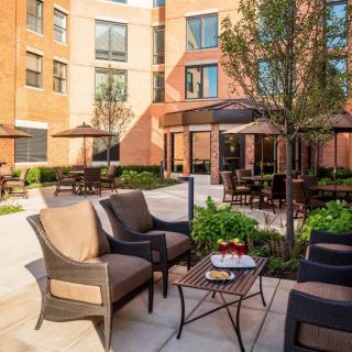 A cozy outdoor patio with seating, surrounded by a brick building and greenery.