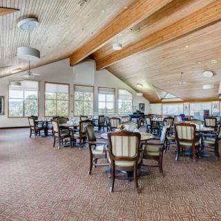 A spacious and well-lit dining area with multiple tables and chairs, featuring large windows and a wooden ceiling.