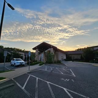 A peaceful sunset over a building, with a clear sky filled with clouds and an empty parking lot.