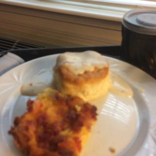 A delicious breakfast featuring a flaky biscuit topped with gravy and a slice of savory casserole.