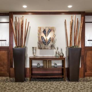 A stylish interior featuring tall vases with decorative sticks, a central wooden console table adorned with books and beverages, and a piece of modern artwork on the wall.