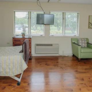 A simple hospital room with a bed, television, and green armchair.