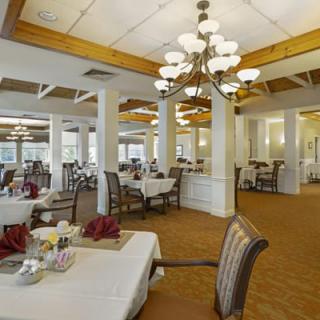 An elegant dining room with neatly arranged tables and chairs, illuminated by chandeliers.
