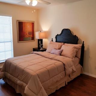 A cozy bedroom with a neatly made bed, bedside lamp, and artwork on the wall.