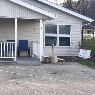 A quaint house with a small porch and blue chairs, featuring a sign on the driveway.