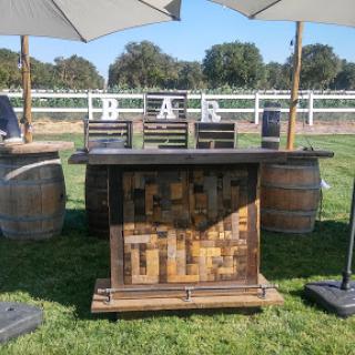 A beautifully arranged outdoor bar setup with a rustic wooden counter and barrels, perfect for an event.