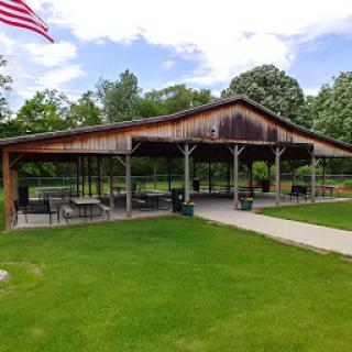 A scenic view of a wooden pavilion with seating, surrounded by lush greenery and an American flag waving in the breeze.
