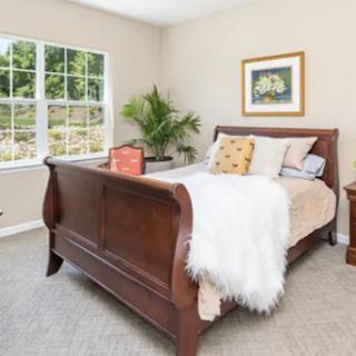 A cozy and inviting bedroom featuring a wooden sleigh bed, adorned with soft bedding and natural light streaming in through large windows.