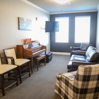 A cozy living room with a piano, chairs, sofa, and television.