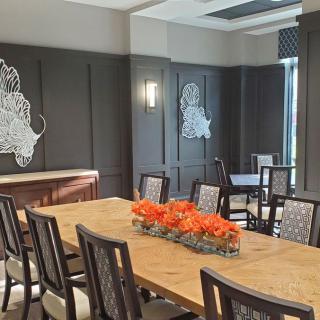 A modern dining or conference room with a large table, surrounded by chairs and decorated with vibrant orange flowers.