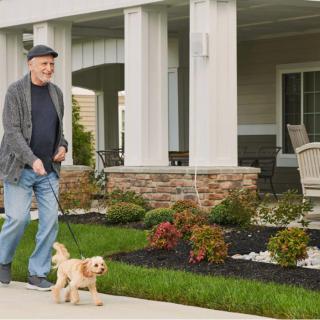 A man walking his dog on a sidewalk in front of a house.