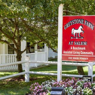 Sign for Graystone Farm at Salem, a senior living community, surrounded by trees and a white fence.