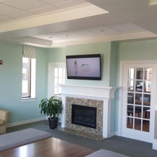 A bright and modern living room featuring a cozy fireplace, a wall-mounted television, and natural light from the windows.