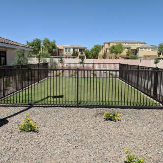 A fenced backyard with a small garden surrounded by a rocky landscape and residential houses in the background.