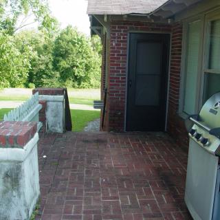 A backyard patio with a brick floor and a grill next to a door.
