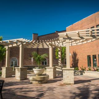 A peaceful courtyard featuring a pergola and a fountain in front of a brick building.