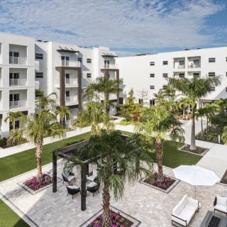 A modern apartment complex featuring a landscaped courtyard with palm trees and outdoor seating.