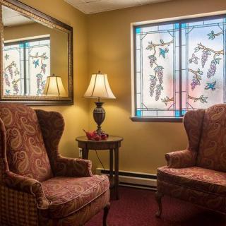 A cozy living room with two armchairs, a lamp, and a stained glass window.