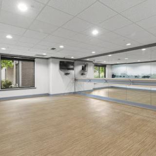A spacious dance studio featuring a large mirror, bright lighting, and a wooden floor, ideal for practice and classes.