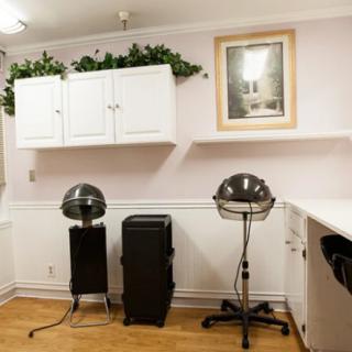 A cozy hair salon interior featuring hair dryers, chairs, and white cabinetry against soft-colored walls.