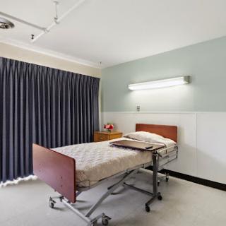 A hospital patient room featuring a bed, gray curtains, and overhead lighting.