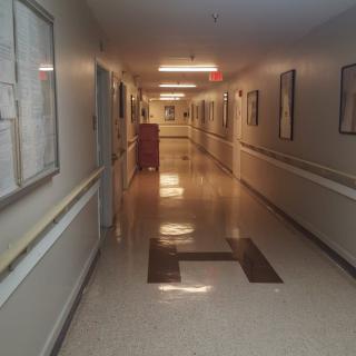 An empty hospital corridor with tiled flooring and overhead lighting.