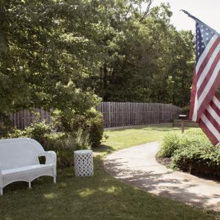 A peaceful backyard scene with a white bench and an American flag.