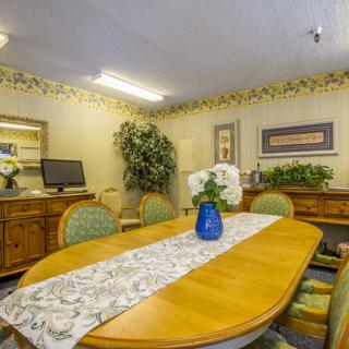 A cozy dining room with a wooden table adorned with a floral centerpiece and surrounded by chairs, complemented by decorative elements in the background.