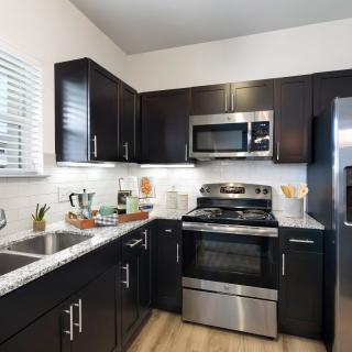 A modern kitchen with dark cabinets and stainless steel appliances.