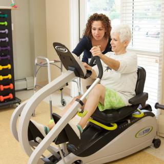 A senior woman receives guidance on using exercise equipment from a therapist.