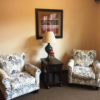 A cozy corner featuring two patterned armchairs and a lamp on a small table, with artwork hanging on the wall.