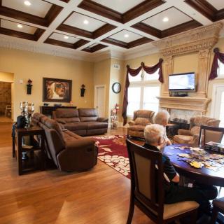 A spacious living room with elegant furnishings, featuring a fireplace and a person seated at the dining table.