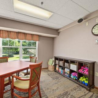 A conference room with a table, chairs, shelving units, and a clock on the wall, illuminated by natural and indoor lighting.